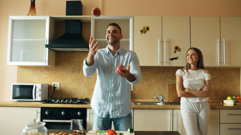 Attractive loving couple having fun in the kitchen. Handsome man juggle with apples to impress his girlfriend at home