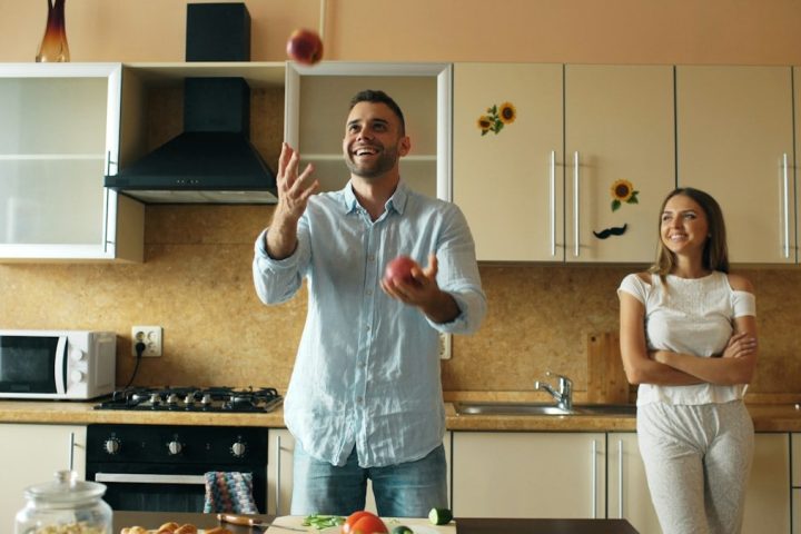 Attractive loving couple having fun in the kitchen. Handsome man juggle with apples to impress his girlfriend at home