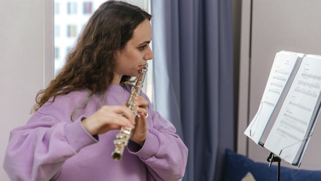 Side view of a woman playing the flute, reading sheet music, indoors.